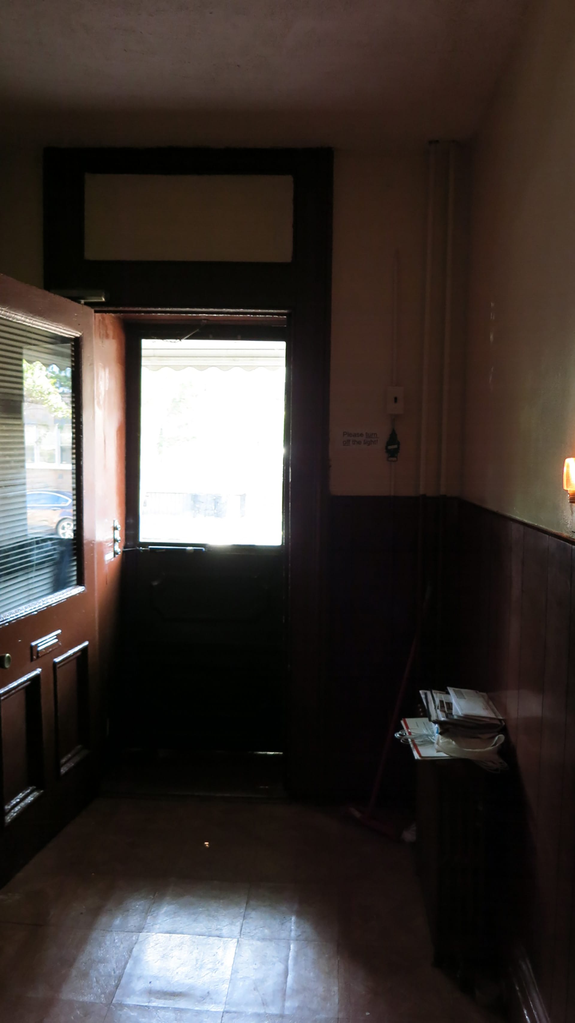 Dark entryway of a Greenpoint home before our renovation with dark wood paneling, door, and floors.